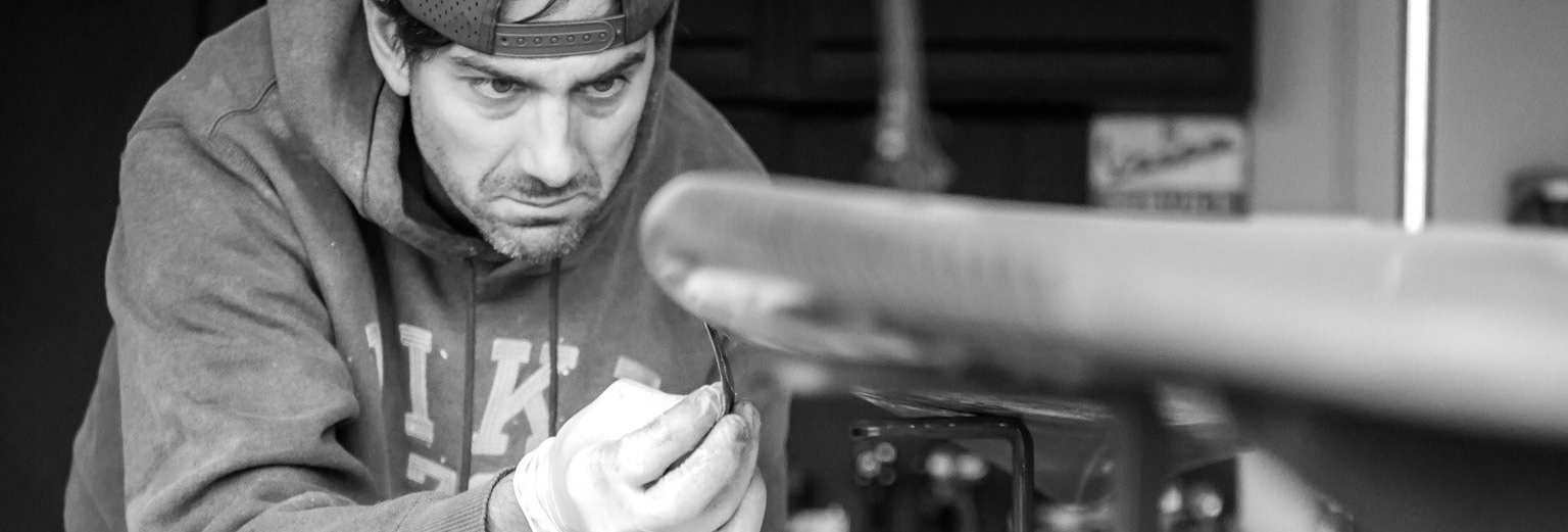 Man wearing a cap a hoodie, working on his surfboard using the G-Force Shaping Rack